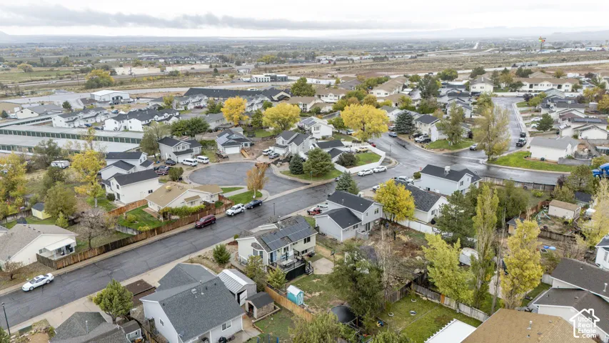 Aerial perspective of a residential neighborhood featuring asphalt-paved streets, mature deciduous trees, fenced rear yards, and solar panels