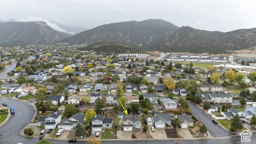 Aerial perspective of a detached residential property featuring a shingled roof, roof-mounted solar panels, an attached garage, and a backdrop of mountain scenery