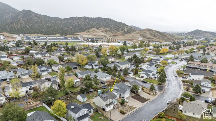Aerial perspective featuring a two-story residence with a concrete driveway, rooftop solar panels, and mountain terrain backdrop
