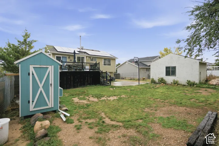 Backyard featuring an elevated deck with black railings, roof-mounted solar panels, a detached structure, and a secondary storage unit