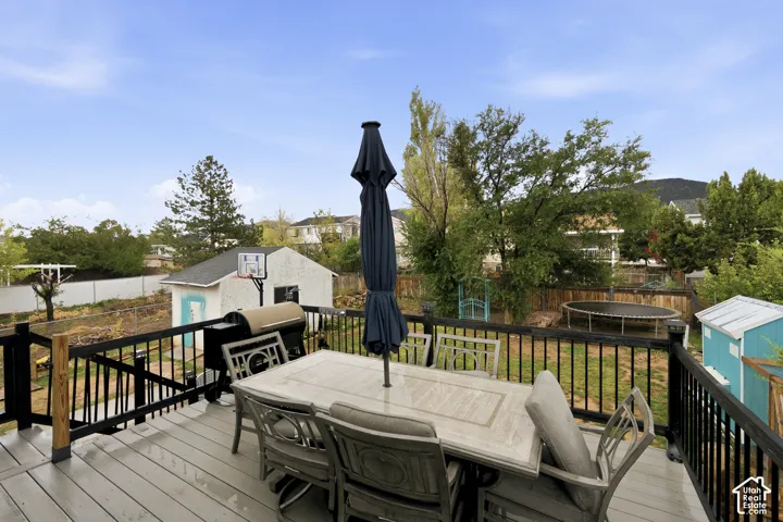 Elevated composite deck featuring black metal railings, overlooking a fenced backyard with mature trees and mountain scenery