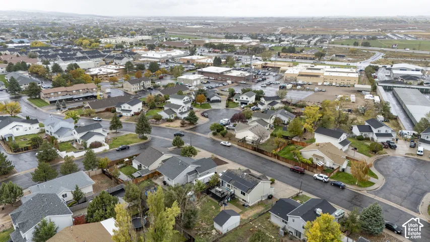 Aerial perspective of a suburban neighborhood featuring residential dwellings, paved street infrastructure, established trees, and surrounding commercial development