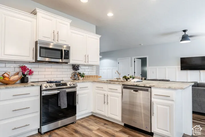Kitchen featuring white cabinetry, stone-surface countertops, subway tile backsplash, stainless steel appliances, and wood-finish flooring