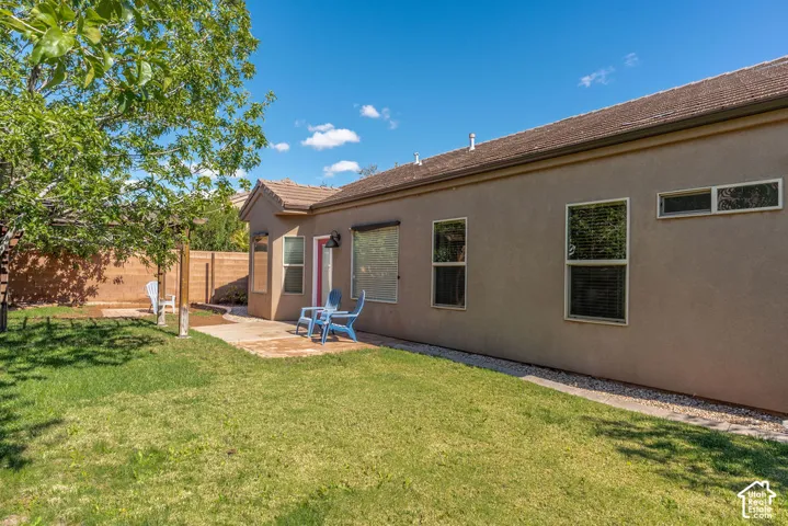 Rear exterior featuring a stucco facade, concrete patio, wooden pergola, perimeter masonry wall, and a sod lawn