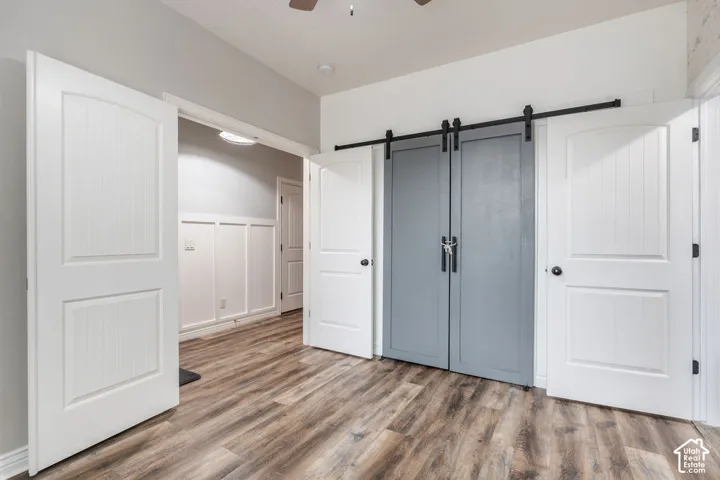 Room interior featuring wood-finish flooring, grey double barn doors on a black sliding rail system, white three-panel interior doors, and wainscoting detail