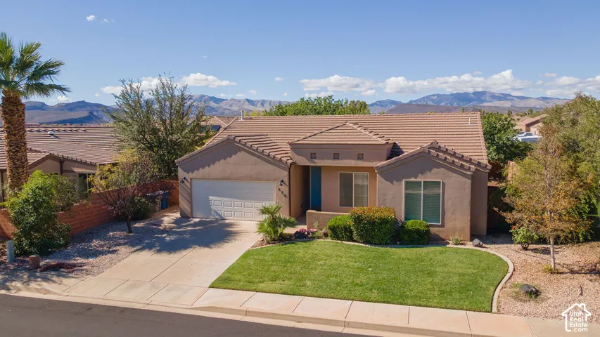 Single-level residence with stucco exterior, tile roofing, attached two-car garage, manicured front lawn, and mountain backdrop