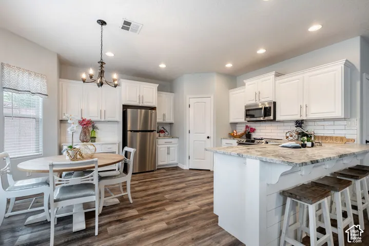 Kitchen featuring white cabinetry, stone countertops, a subway tile backsplash, a center island with plank-style detail, and wood-finish flooring
