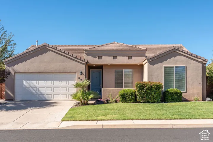 Stucco exterior featuring a tile roof, recessed entryway, attached two-car garage, and front landscaping
