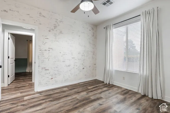 Room featuring a whitewashed brick accent wall, wood-finish flooring, and a ceiling fan with integrated lighting