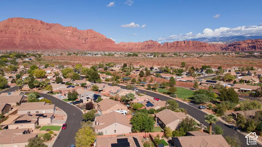 Aerial perspective of a residential neighborhood featuring prominent red rock mountain scenery, paved streets, and homes with installed solar panel arrays