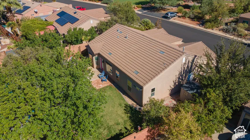 Stucco exterior residence featuring a tile roof, brick-paved patio, manicured lawn, mature trees, and an enclosed yard
