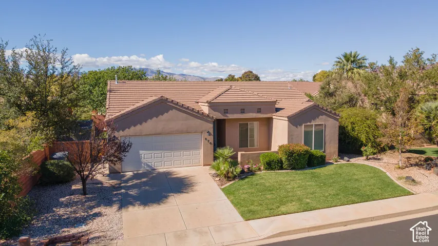 Stucco exterior featuring a tile roof, an attached two-car garage, and manicured front lawn landscaping