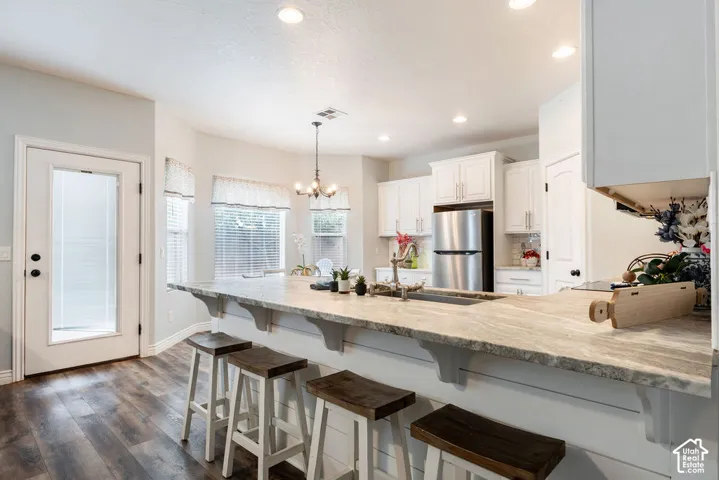 Kitchen featuring an expansive stone countertop, shaker-style cabinetry, stainless steel appliances, wood-finish flooring, and shiplap detailing on the breakfast bar