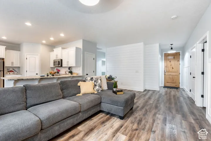 Open-concept area featuring wood-finish flooring, white shiplap accent wall, recessed lighting, and kitchen with stone countertops and white cabinetry