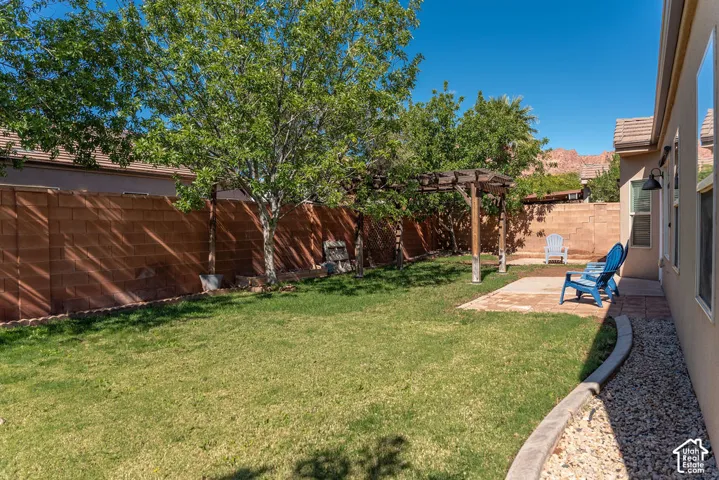 Backyard featuring a paved stone patio, wood pergola, grass lawn, and masonry perimeter wall, set against a mountain backdrop