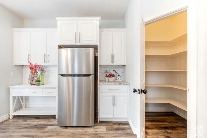 White shaker-style cabinetry, stainless steel refrigerator, stone-surface countertop, subway tile backsplash, and walk-in pantry with built-in shelving