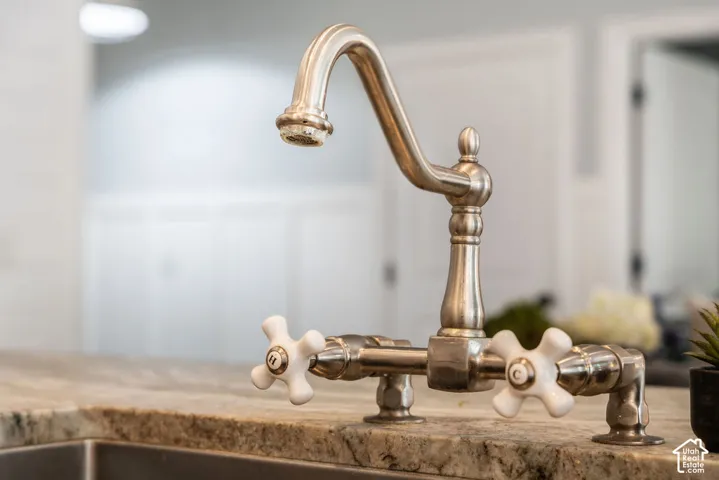 Bridge-style faucet with a brushed metallic finish, ceramic cross-handle controls, and a high-arch swivel spout, mounted on a stone-surface countertop
