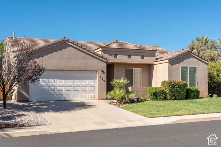 Stucco exterior with a tiled roof, integrated two-car garage, concrete driveway, and landscaped front lawn with mature shrubbery