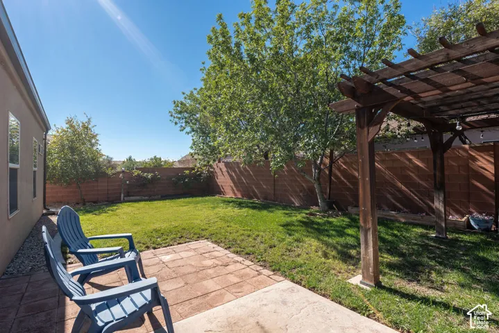 Backyard featuring a paved stone patio, a wooden pergola, a manicured lawn, and perimeter masonry wall fencing