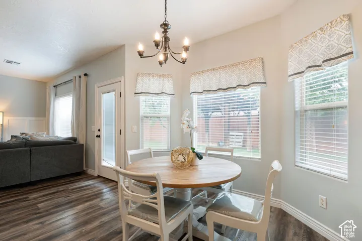 Dining area featuring wood-finish flooring, a multi-arm metal chandelier, and a bay window configuration with horizontal blinds