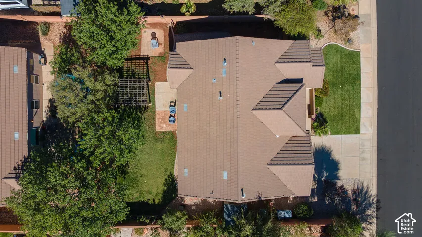 Aerial perspective of a property featuring a tile roof, paved driveway, dedicated pergola structure, and landscaped grounds with mature trees