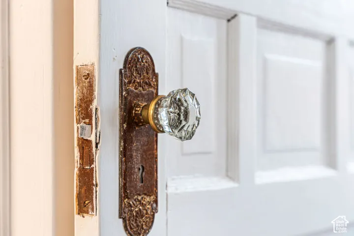 Multi-panel white door featuring an antique brass hardware plate with intricate embossed detailing and a faceted glass knob
