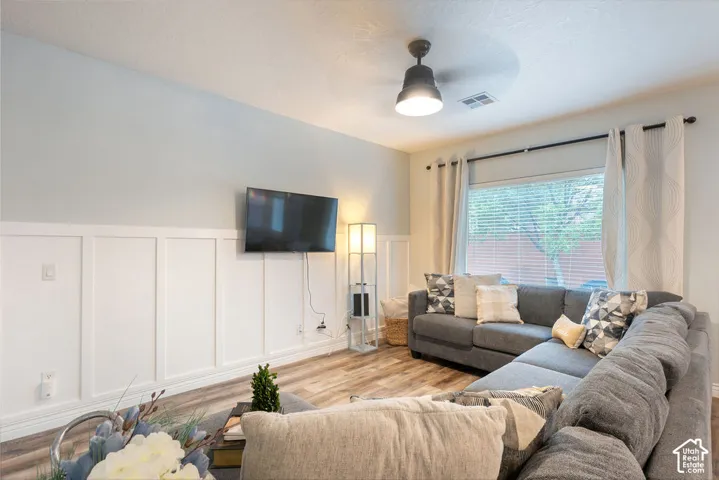 Wood-finish flooring, white board-and-batten wall detailing, and a modern ceiling fan with integrated lighting