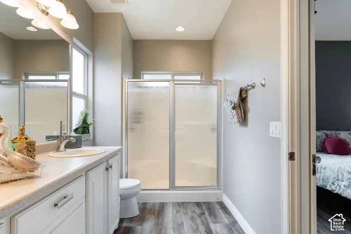 Bathroom featuring a vanity with a solid-surface countertop, integrated basin, brushed metal hardware, and wood-finish flooring, including a shower with a metal-framed frosted glass enclosure