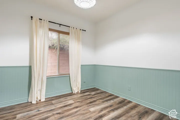 Room featuring wood-finish flooring, half-wall beadboard wainscoting, a single-pane window, and a flush-mount circular ceiling light fixture