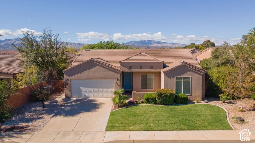 Single-story residence featuring a tile roof, stucco exterior, two-car garage, manicured front lawn, and mountain backdrop