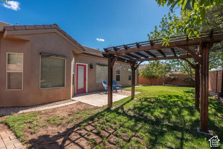 Stucco exterior featuring a wood pergola, concrete patio, grass lawn, and wood privacy fencing