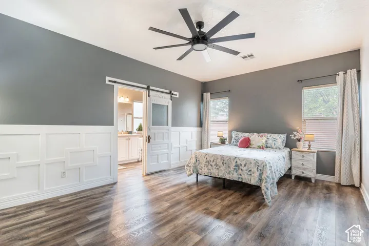 Room featuring wood-finish flooring, white grid-pattern wainscoting, matte black ceiling fan, and white barn-style sliding door with glass inlay