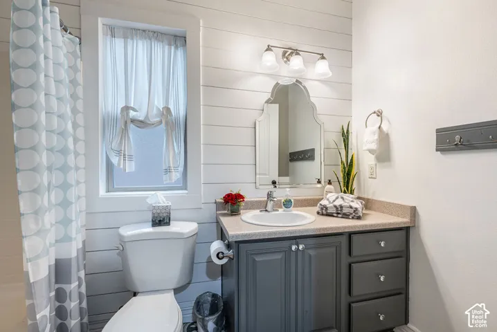 Bathroom featuring horizontal plank wall paneling, charcoal-finished vanity cabinet, solid-surface countertop with integrated basin, decorative arched mirror, and three-bulb vanity lighting