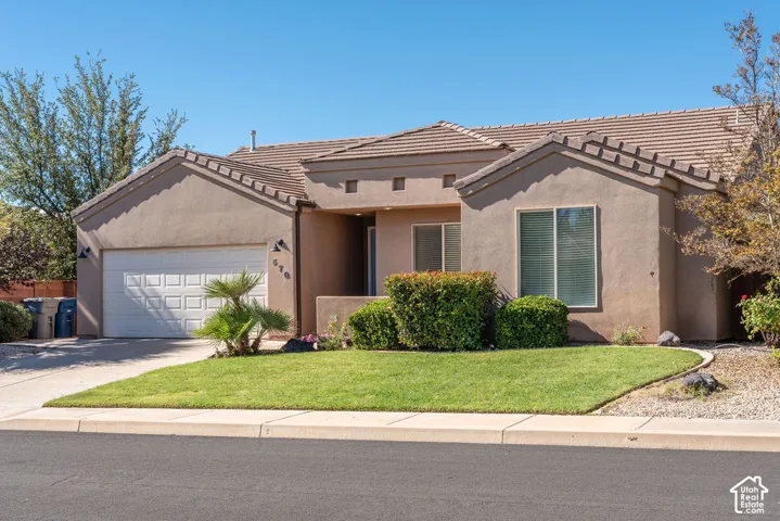 Stucco exterior featuring a tile roof, an attached two-car garage, and manicured landscaping