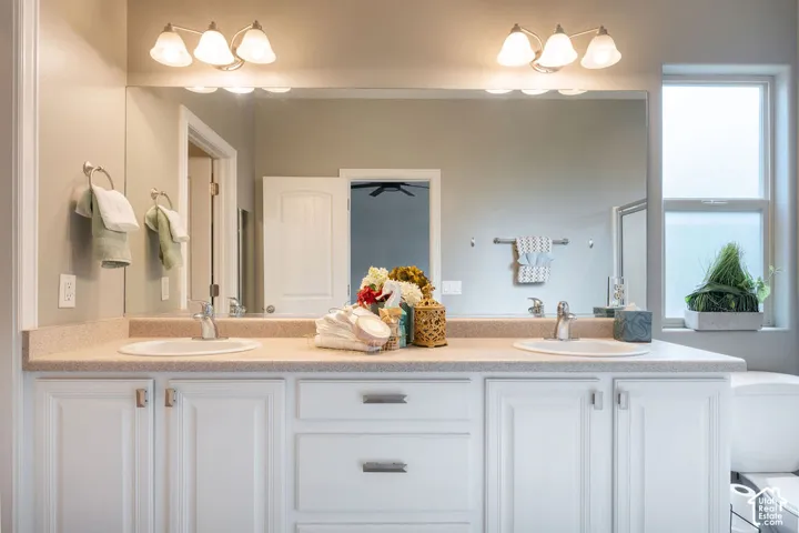 Double-sink vanity featuring a solid-surface countertop, white cabinetry with brushed-metal hardware, a full-width wall mirror, and two dual-bulb vanity light fixtures