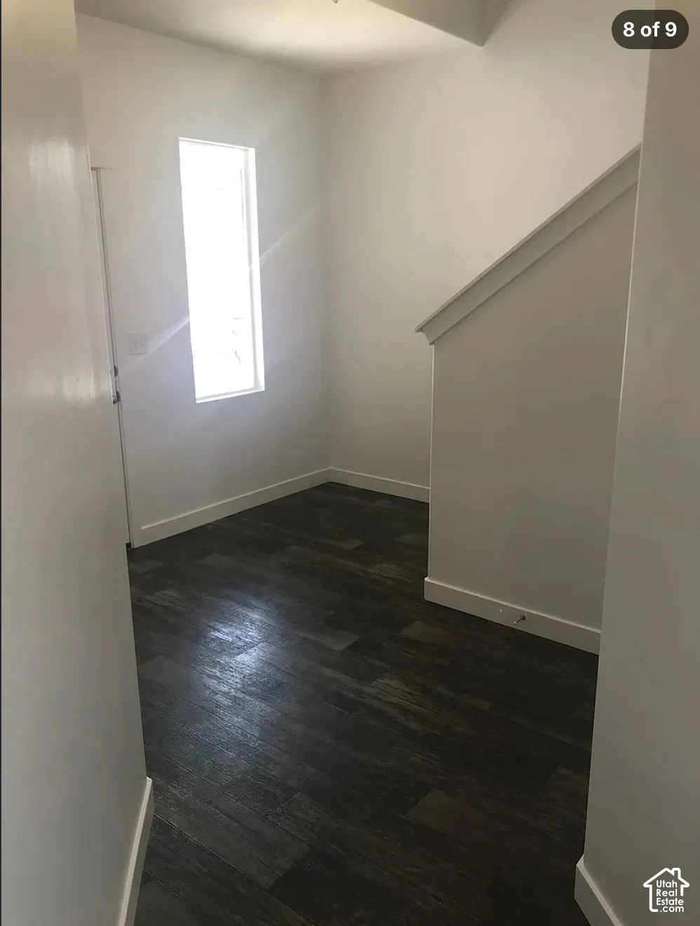 Wood-finish flooring, vertical rectangular window, and architectural stairway wall