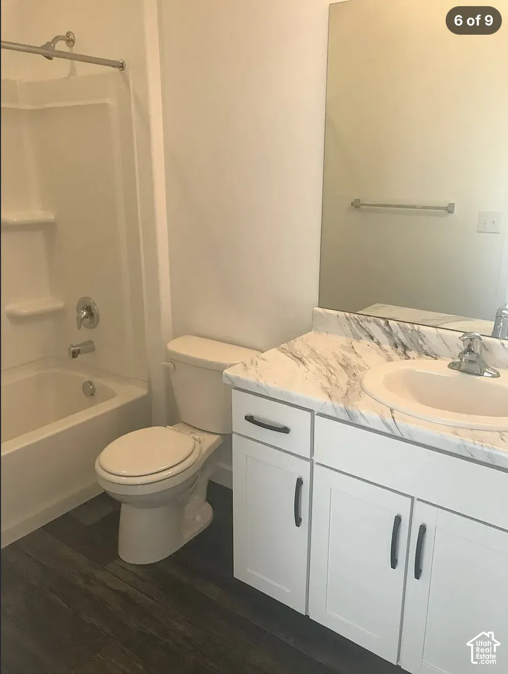 Bathroom featuring a vanity with a white countertop and integrated basin, white shaker-style cabinetry with matte black hardware, wood-finish flooring, and a tub-shower combination with built-in shelving