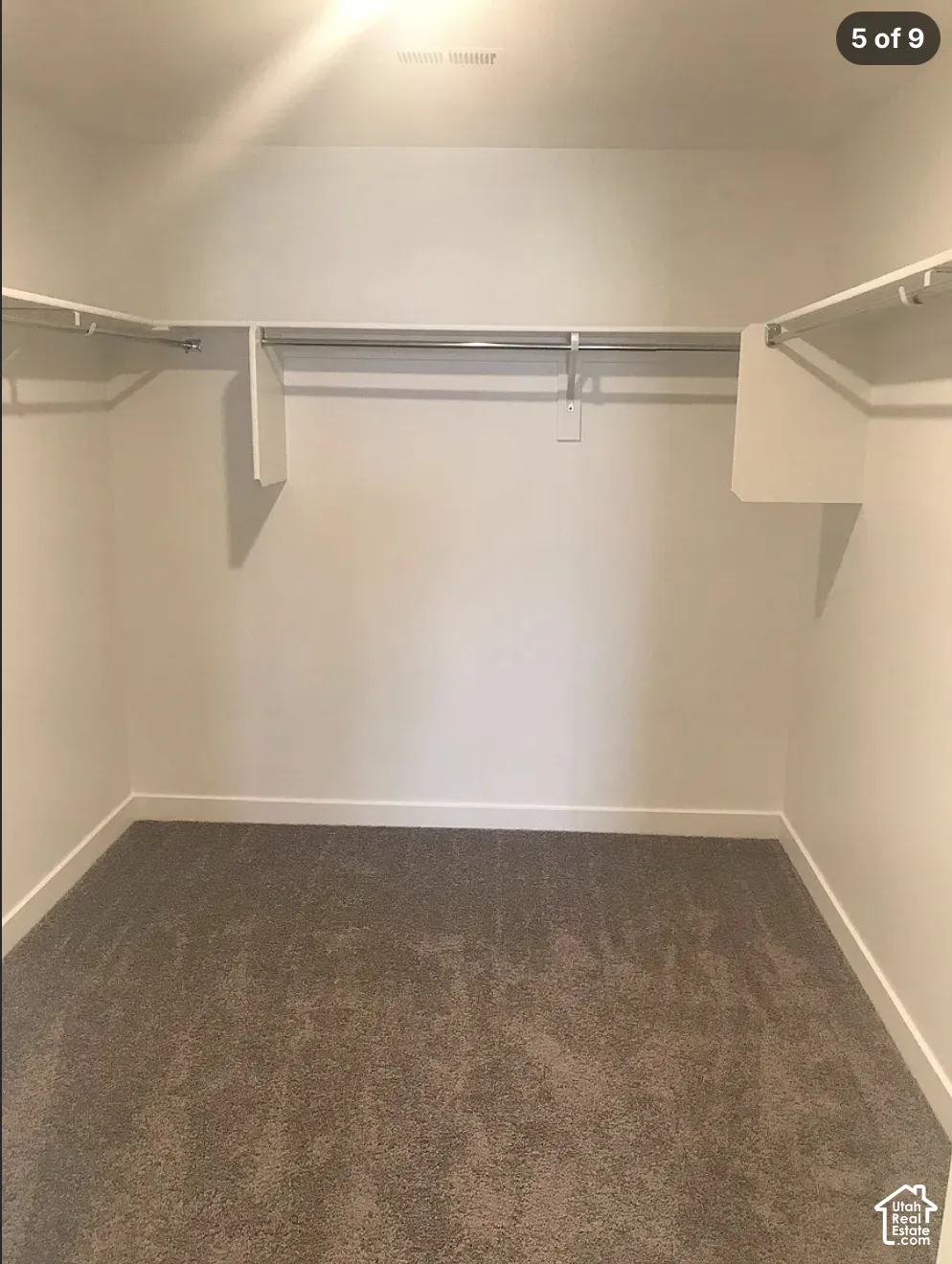 Walk-in closet featuring neutral carpeting and built-in tiered shelving with integrated hanging rods