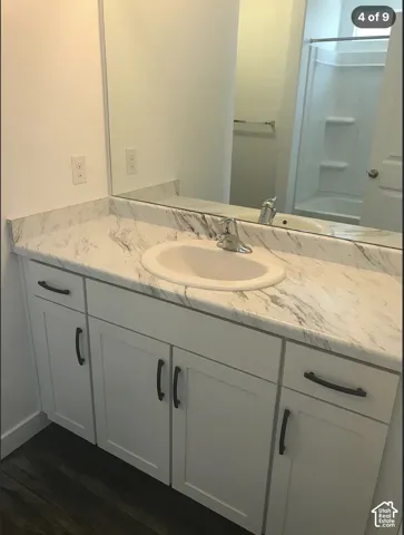 Bathroom vanity featuring white cabinetry, dark hardware, integrated surface with a drop-in sink, and a full-width mirror