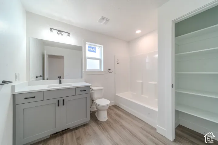 Bathroom featuring a grey vanity with a white countertop, integrated sink, wood-finish flooring, a combination tub and shower surround, and built-in shelving