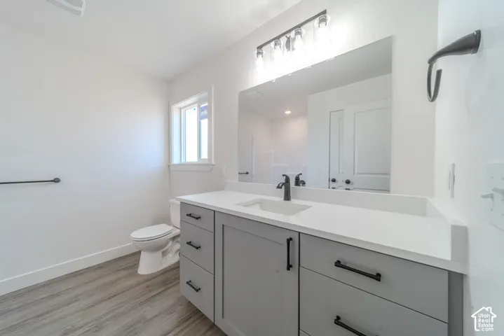Bathroom featuring a gray shaker-style vanity with white countertop, integrated rectangular sink, matte black hardware, and wood-finish flooring