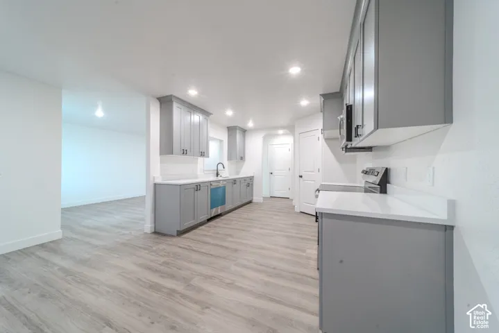 Kitchen featuring grey shaker-style cabinetry, quartz countertops, integrated stainless steel appliances, recessed lighting, and wood-finish flooring