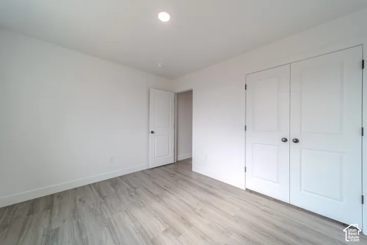 Neutral-toned wood-finish flooring, white walls, recessed ceiling lighting, two-panel interior doors, and a double-door closet