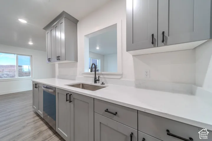 Kitchen featuring grey shaker-style cabinetry, white countertops, a stainless steel undermount sink with a matte black faucet, integrated stainless steel dishwasher, and wood-finish flooring