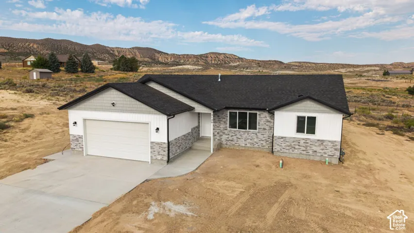 Single-level exterior featuring a multi-material facade of stone veneer, vertical siding, and shingle accents with a dark asphalt shingle roof, concrete driveway, and attached garage