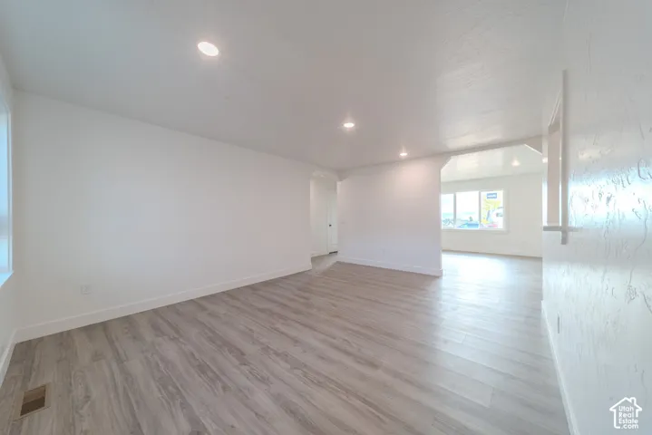Open interior space featuring light-toned wood-finish flooring, smooth white walls, recessed ceiling lighting, and a wide cased opening