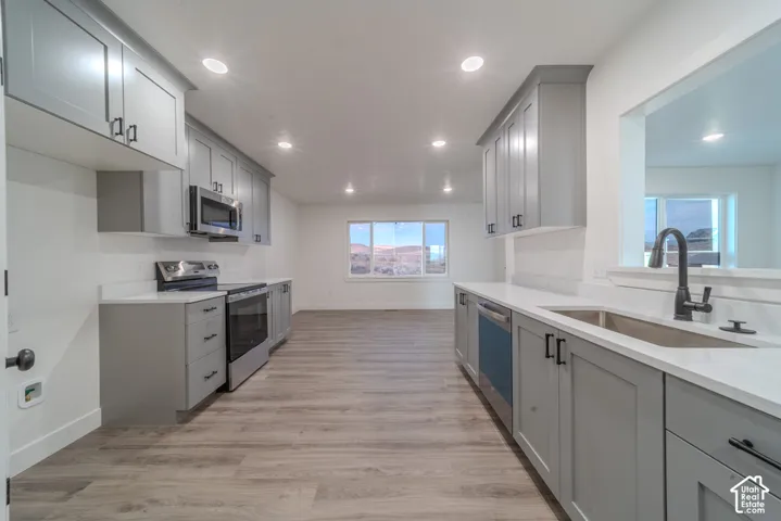 Kitchen featuring grey shaker-style cabinetry, white quartz countertops, stainless steel appliances, wood-finish flooring, and a matte black faucet