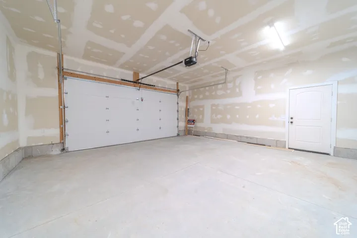 Attached two-car garage featuring a white sectional overhead door, concrete floor, automatic door opener, and a dedicated service door