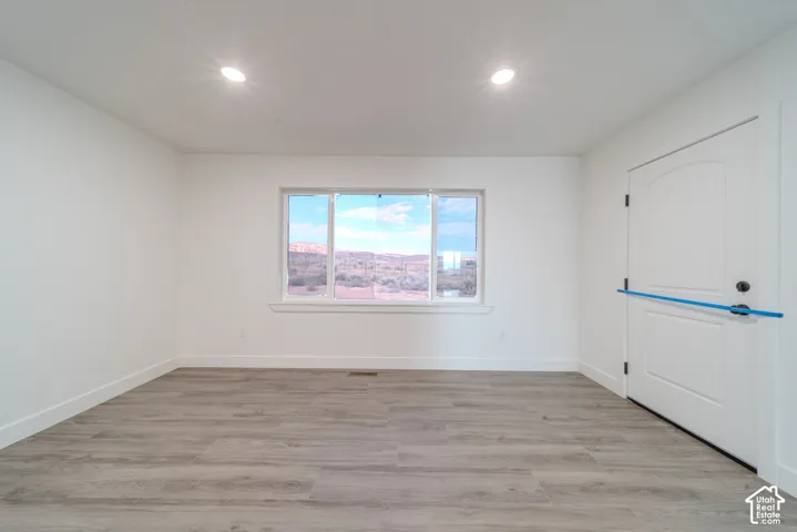 Neutral-toned room featuring wood-finish flooring, recessed lighting, a multi-pane window, and an arched-panel entry door