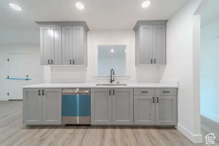 Kitchen area featuring gray Shaker-style cabinetry, white countertops, stainless steel dishwasher, undermount sink with a matte black faucet, and wood-finish flooring